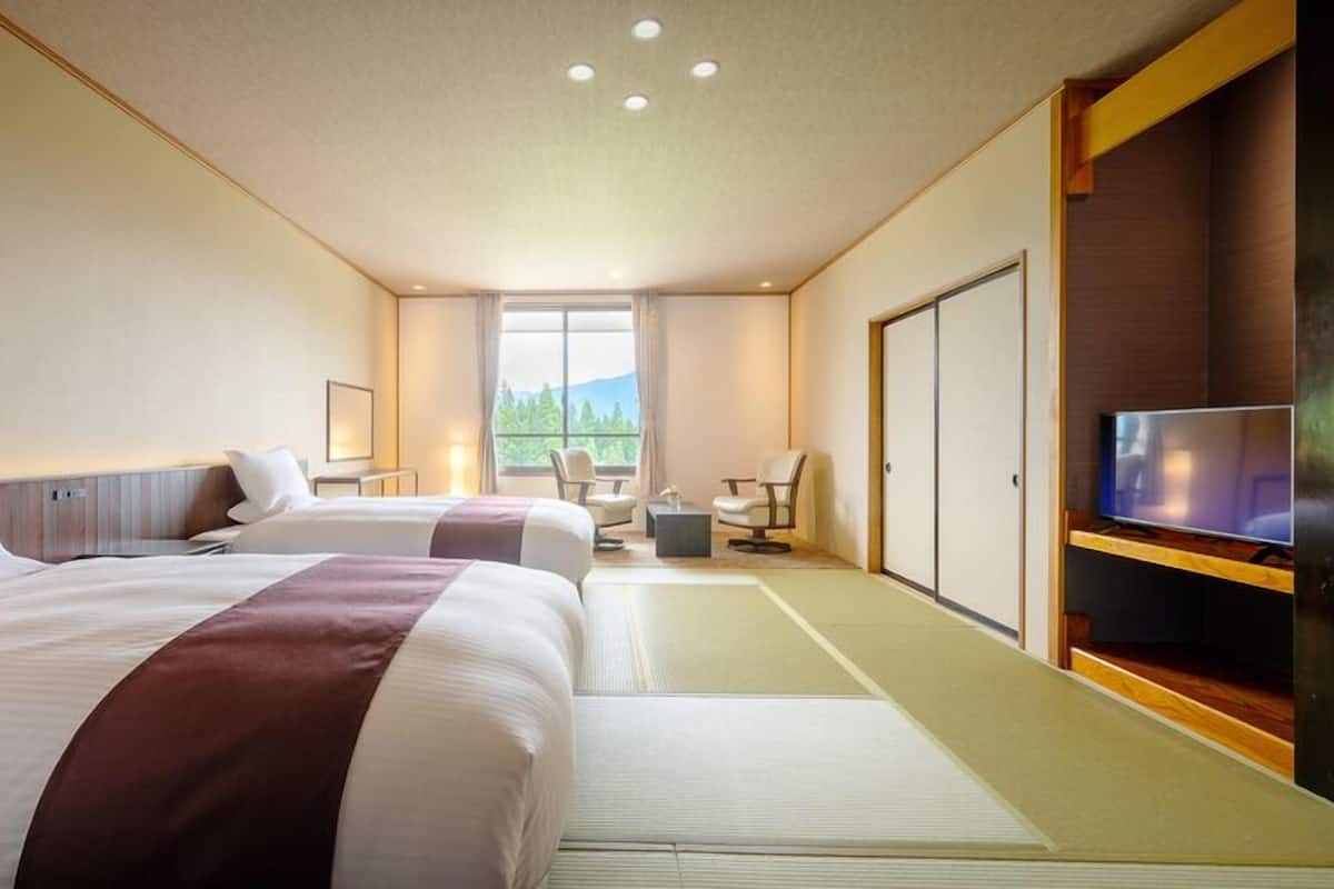 A hotel room with two beds, a TV, a desk, and a view of the outdoors.