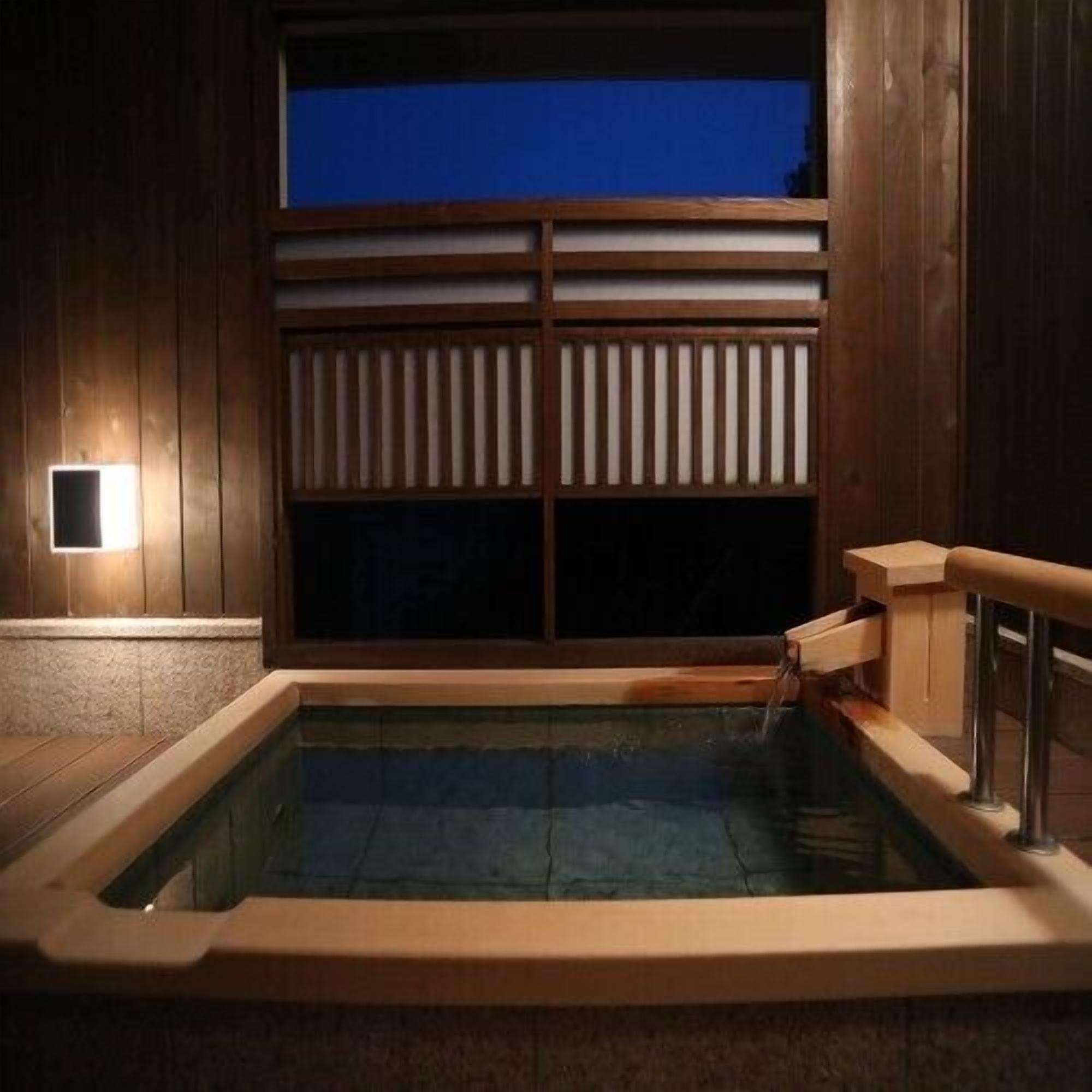 A hot tub with a wooden exterior, a window with blinds, and a small wall-mounted light.