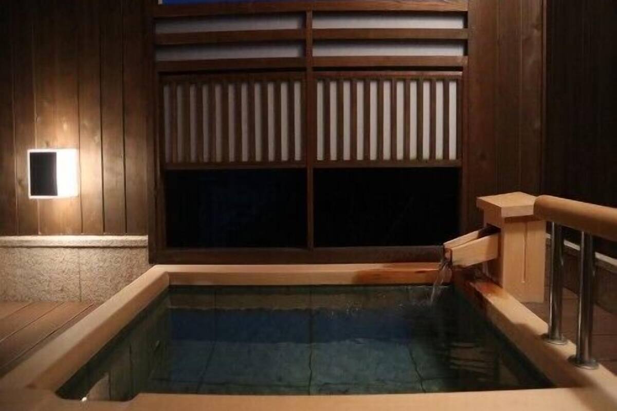 Un jacuzzi con revestimiento de madera, una ventana con persianas y una pequeña luz empotrada.