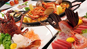 Una bandeja de mariscos con diversos tipos de pescados y mariscos, incluyendo camarones, langosta y almejas, dispuesta sobre un plato blanco con adornos.