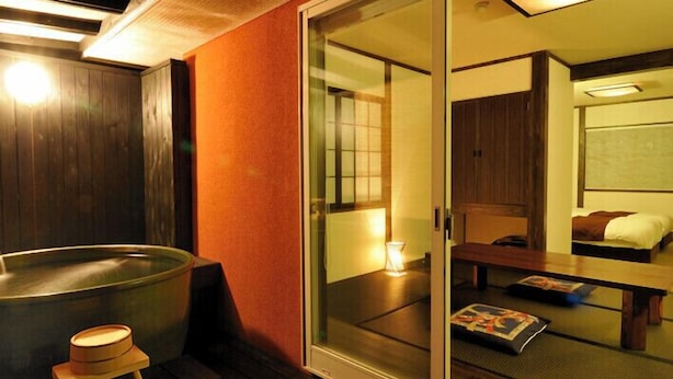 Una habitación de estilo japonés tradicional con piso de madera, una puerta corredera de vidrio que da a un dormitorio y una bañera de madera.