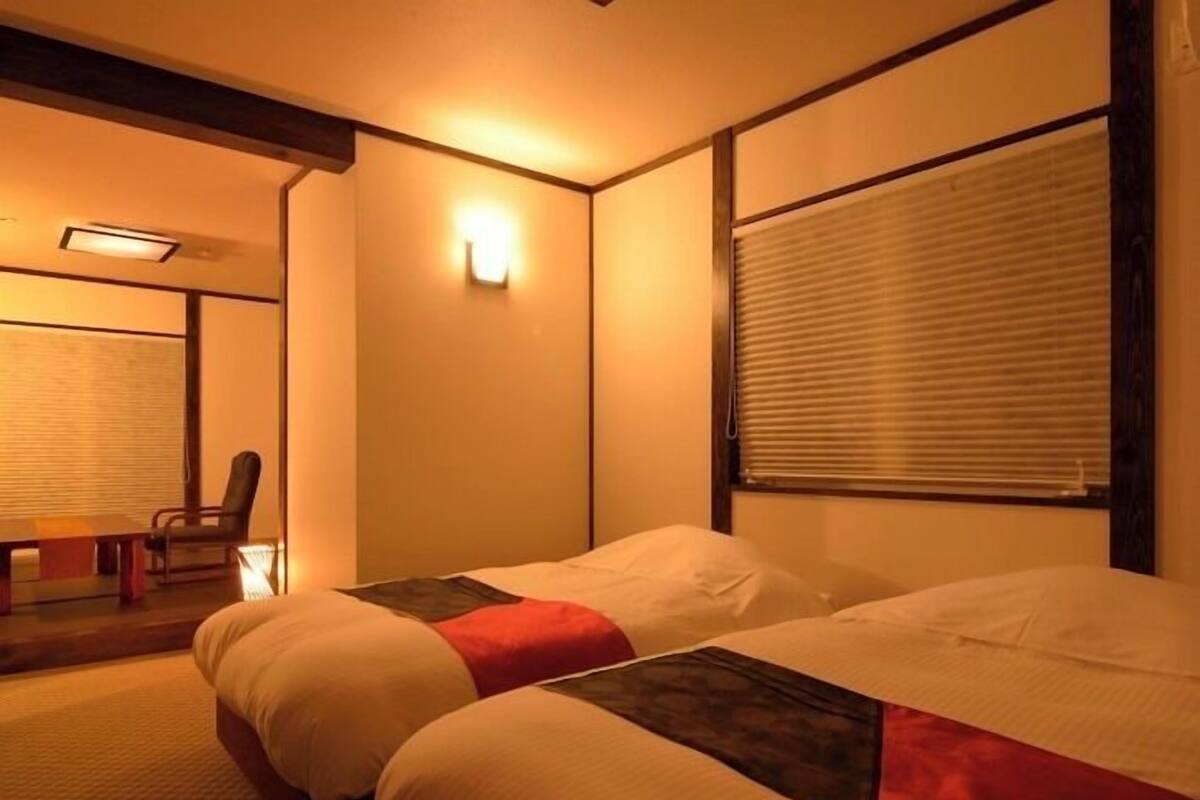 Habitación de hotel con cama, una silla, una mesa y una ventana con persianas.