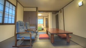 Una habitación japonesa tradicional con suelo de tatami, una mesa de madera baja y un fusuma que conduce a una zona de descanso.