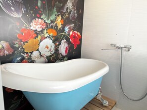 A bathroom with a freestanding bathtub, a shower, and a floral mural on the wall. - Wood Design Park Seto (Hokuto)