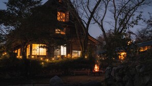 Una cabaña rústica con ventanas amplias, un hoyo para el fuego y un muro de piedra.