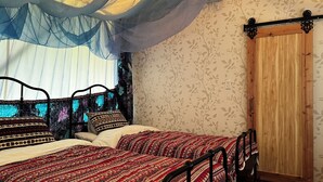 Una habitación con cama, puerta de madera y ventana con cortinas de gasa.