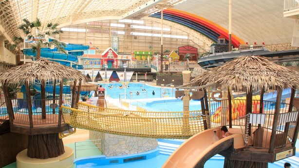 Parque acuático interior con una piscina grande, toboganes y estructuras de juego.