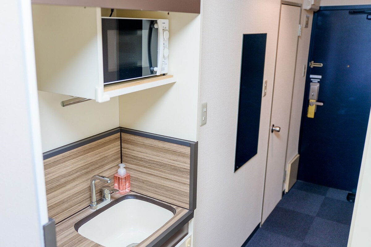 A compact bathroom with a sink, a mirror, and a microwave above it.