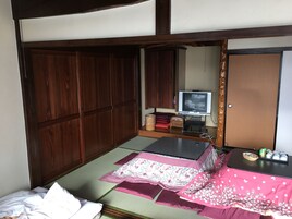 A traditional Japanese-style room with tatami flooring, a futon bed, a television, and a sliding door.