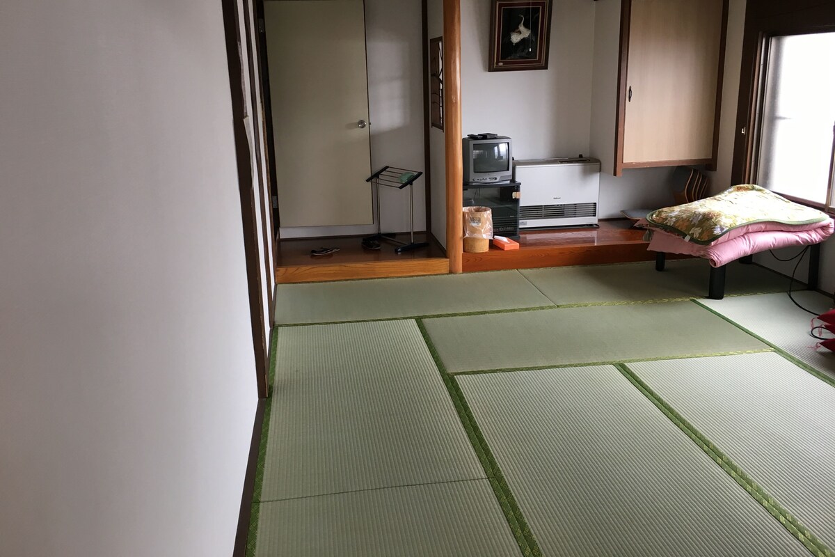 Une pièce de style japonais traditionnel, avec un sol recouvert de tatamis, un futon servant de lit, une télévision et un radiateur.