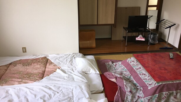 Ein Schlafzimmer mit einem Bett, einer rot-weißen Musterdecke, einem Holzschrank, einem Fernseher und einem kleinen Hocker.