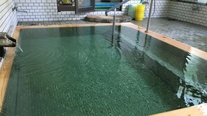 Ein heller, überdachter Pool mit Holzrand, einem sichtbaren Wasserfiltersystem und einer gefliesten Wand im Hintergrund.