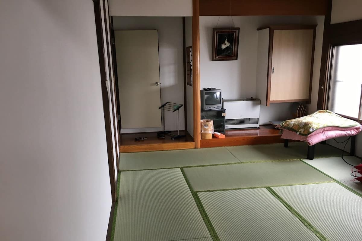 Una habitación japonesa tradicional con suelo de tatami, una cama futón, un televisor y un calentador.