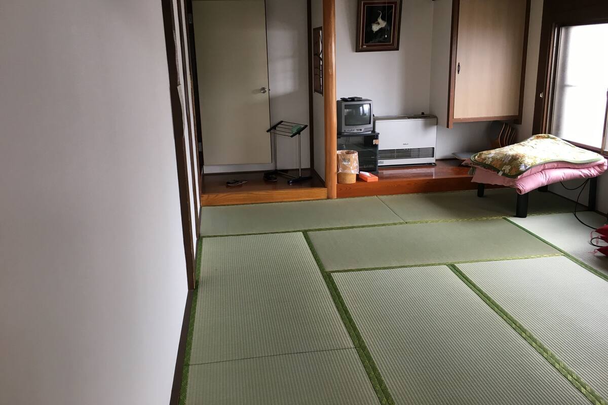Una habitación japonesa tradicional con suelo de tatami, un futón, un televisor y un calentador.