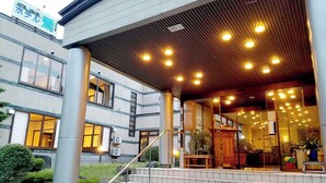 A hotel entrance with a covered walkway, multiple windows, and indoor lighting. - Oshuku Onsen Hotel Uguisu (Shizukuishi)