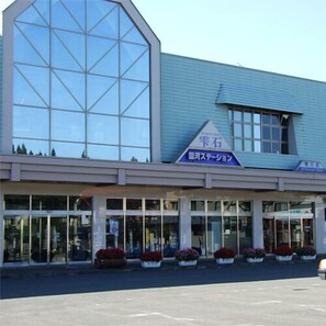 A building with a large glass facade, a sign with Japanese characters, and potted plants in front.