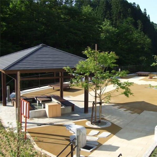 A covered outdoor area with a seating area, a small building, and a tree.
