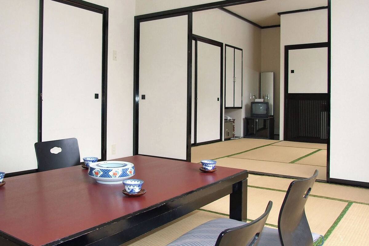 Ein traditioneller japanischer Raum mit Tatami-Bodenbelag, einem Holztisch und einem Fernseher.