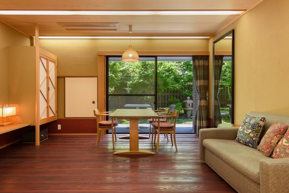 Ein Zimmer mit Esstisch, Stühlen, einer Couch, einem Fernseher und einer Glastür zum Garten.