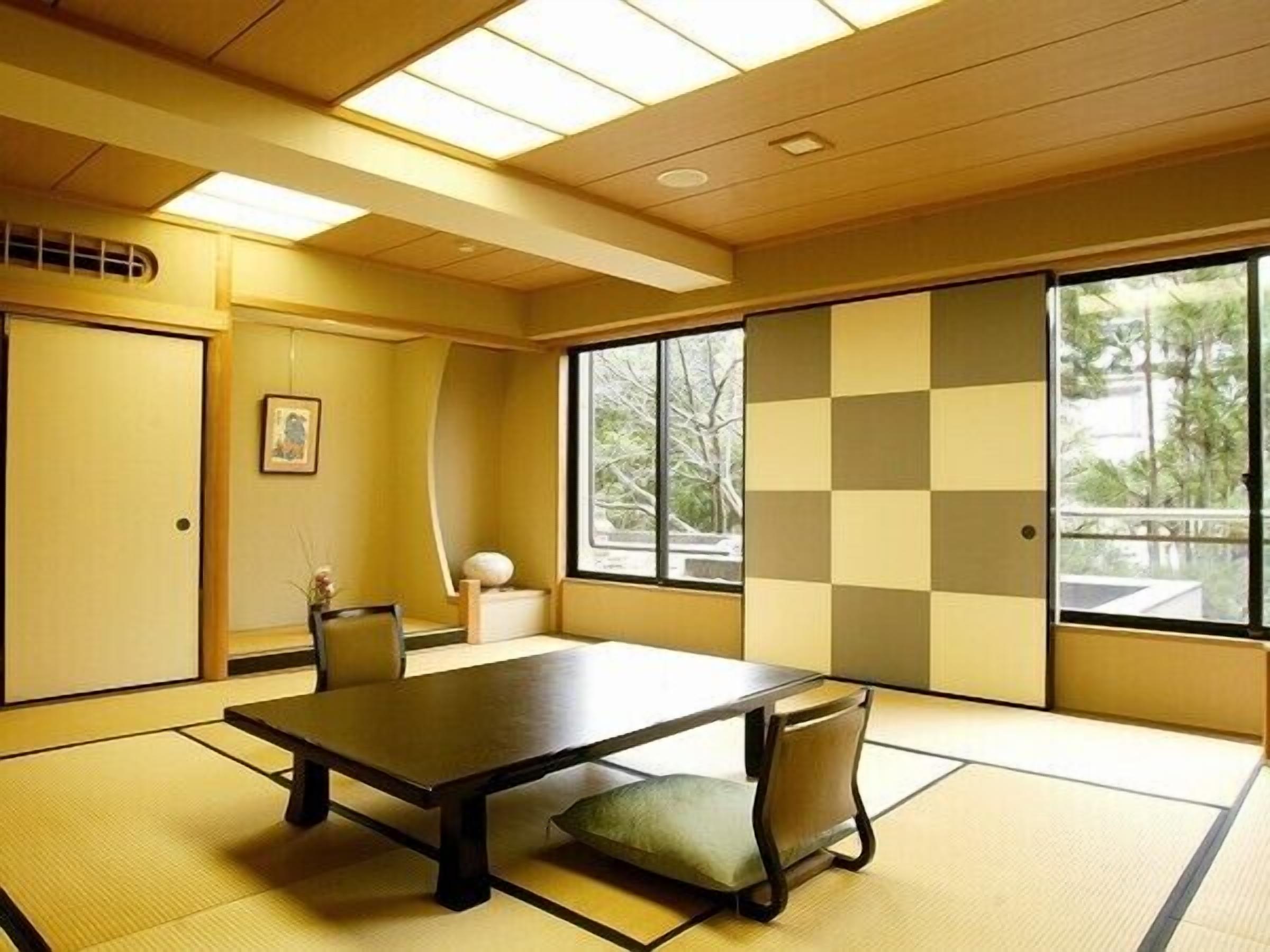 Um espaço com tatames, uma mesa baixa e cadeiras, janelas amplas e uma porta de correr.