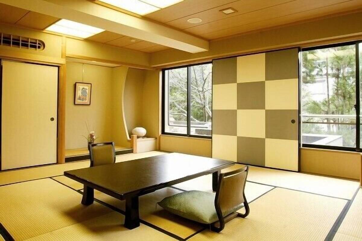 Een kamer met tatami matten, een lage tafel en stoelen, grote ramen en een schuifdeur.