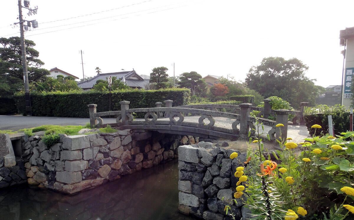 Un puente de piedra sobre un canal, rodeado de vegetación y edificios tradicionales.