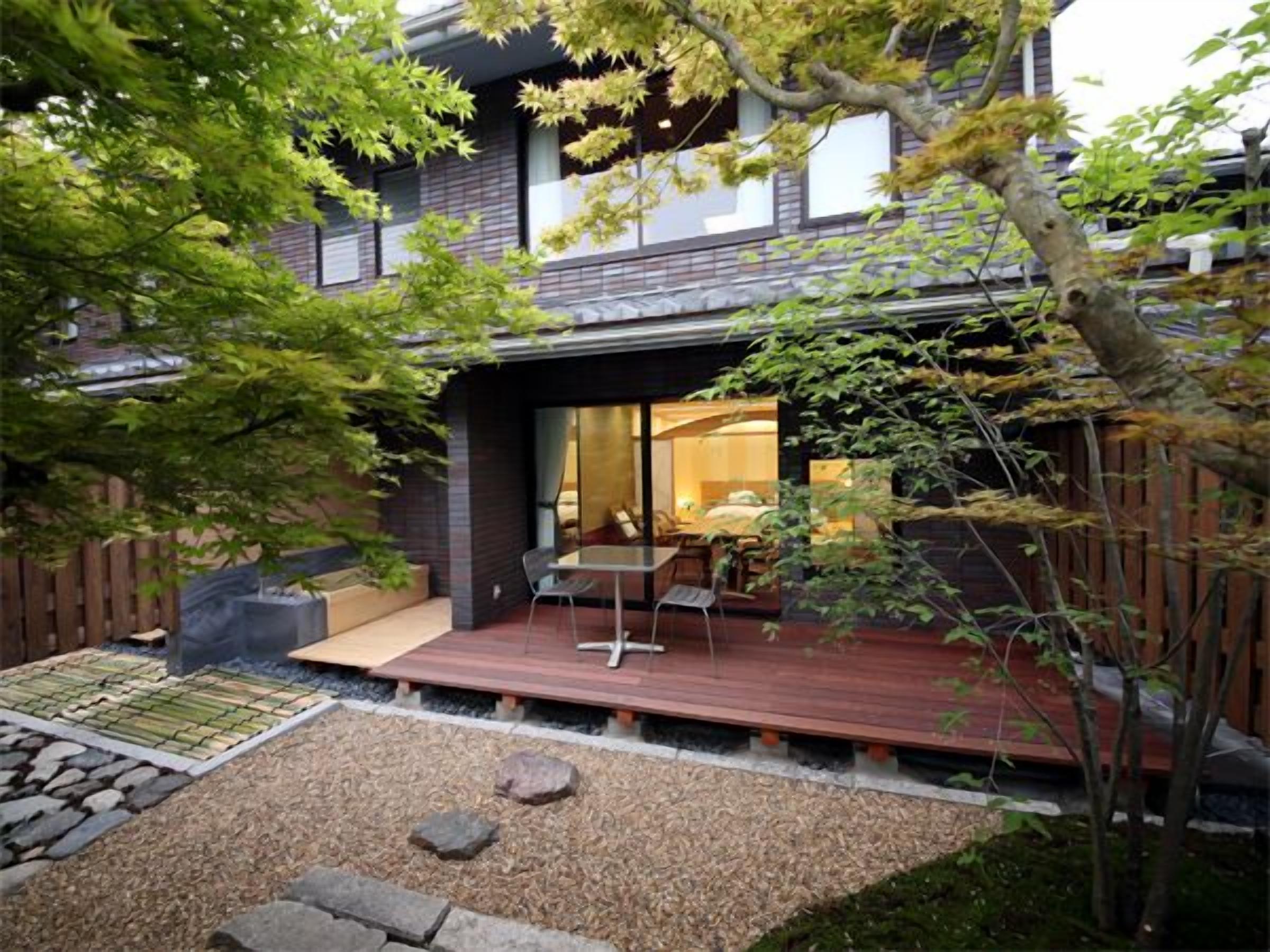A modern house with a deck, a small garden area with rocks, and a wooden fence.