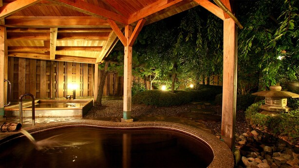 Uma estrutura de madeira com uma banheira de hidromassagem, cercada por um jardim à noite.