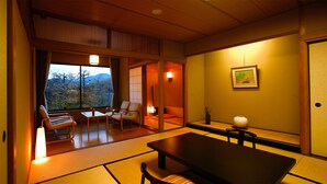 Um quarto japonês tradicional com tatames, uma mesa baixa, cadeiras e uma porta deslizante que dá para uma varanda com vista para as montanhas.