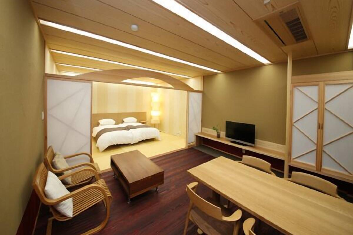 Een hotelkamer met een bed, een televisie, een houten eettafel en een zithoek met stoelen.