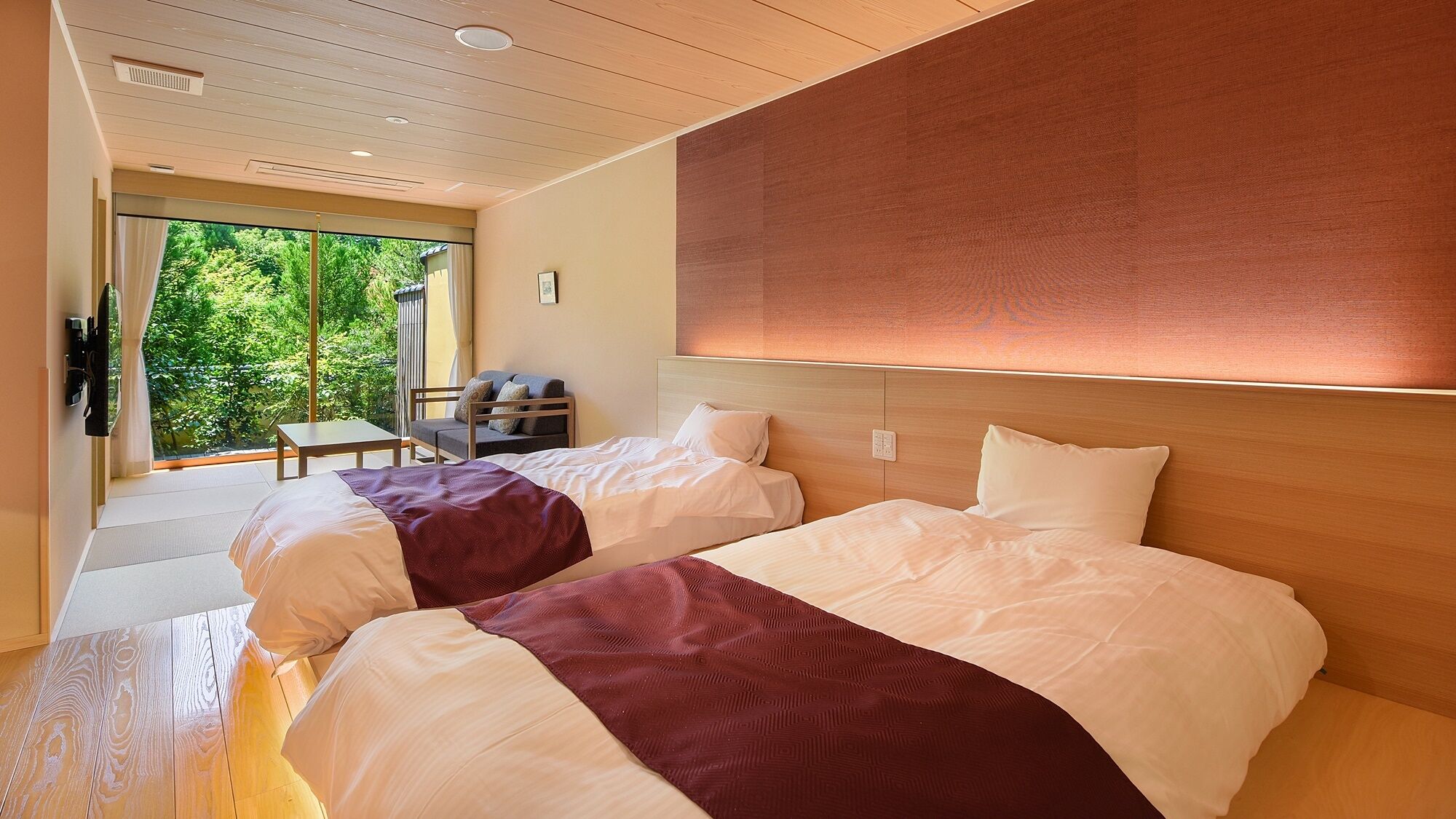 Quarto de hotel com duas camas, um sofá, uma mesa e vista para o verde lá fora.