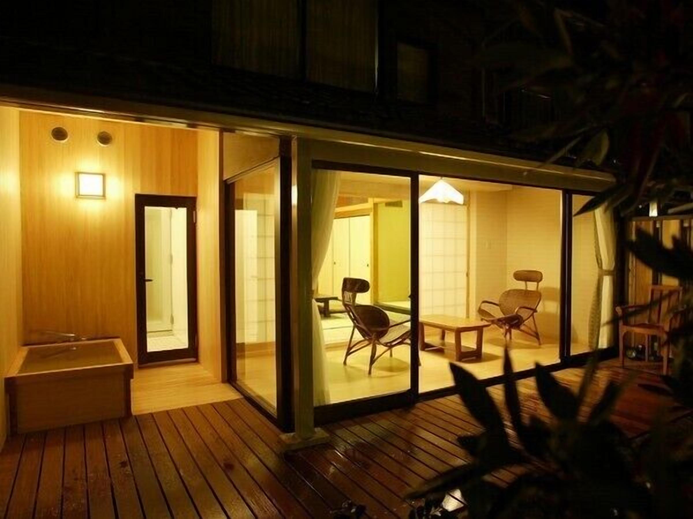 Quarto de hotel moderno com deck de madeira, portas de correr de vidro e área de refeições com cadeiras.