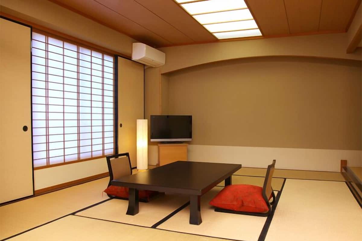 Een traditionele Japanse kamer met tatami vloerbedekking, een lage tafel, een televisie en schuifdeuren.