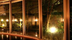 Piscina com deck de madeira, cercada por paredes de vidro e iluminada por luzes externas.