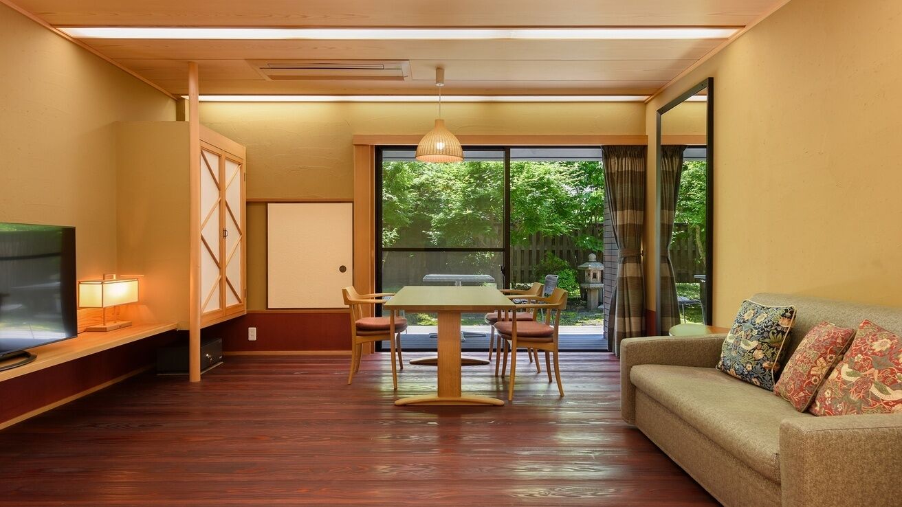 Quarto com uma mesa de jantar, cadeiras, sofá, televisão e uma porta de vidro deslizante para um jardim.