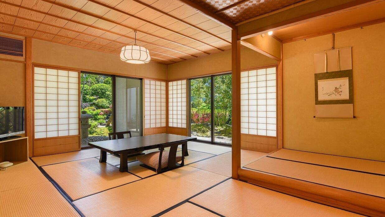 Ein traditioneller japanischer Raum mit Tatami-Böden, einem niedrigen Tisch, Schiebetüren und Blick auf Grünflächen.