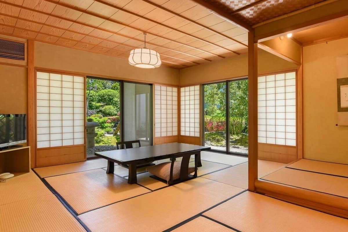 Een traditionele Japanse kamer met tatami vloerbedekking, een lage tafel, schuifdeuren en uitzicht op groen.