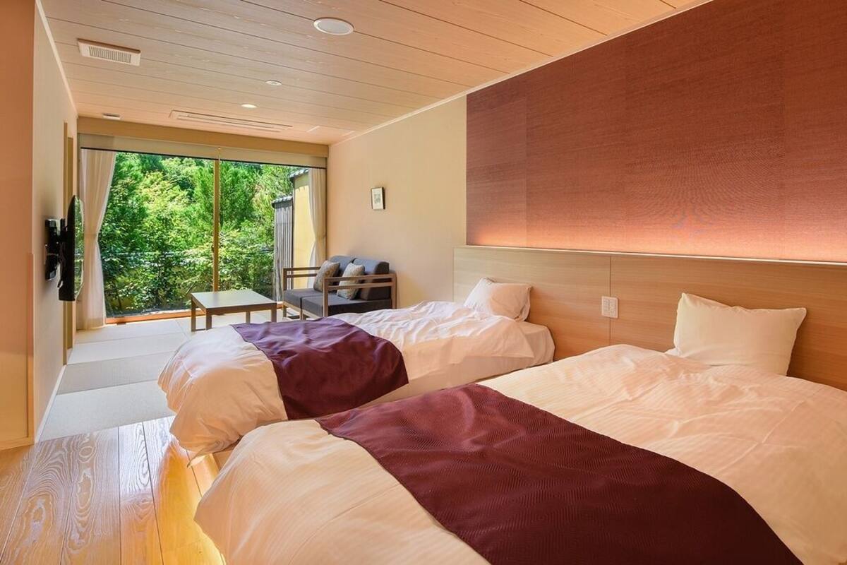 Een slaapkamer met twee bedden, een slaapbank, een televisie en een raam met uitzicht op groen.