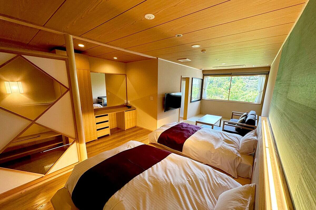 Hotelkamer met twee bedden, een bureau, een stoel, een televisie en een raam met uitzicht op groen.