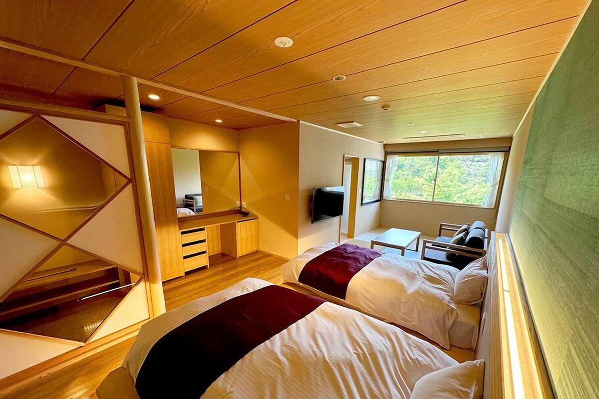 Een kamer met twee bedden, een bureau, een spiegel, een televisie en een raam met uitzicht.