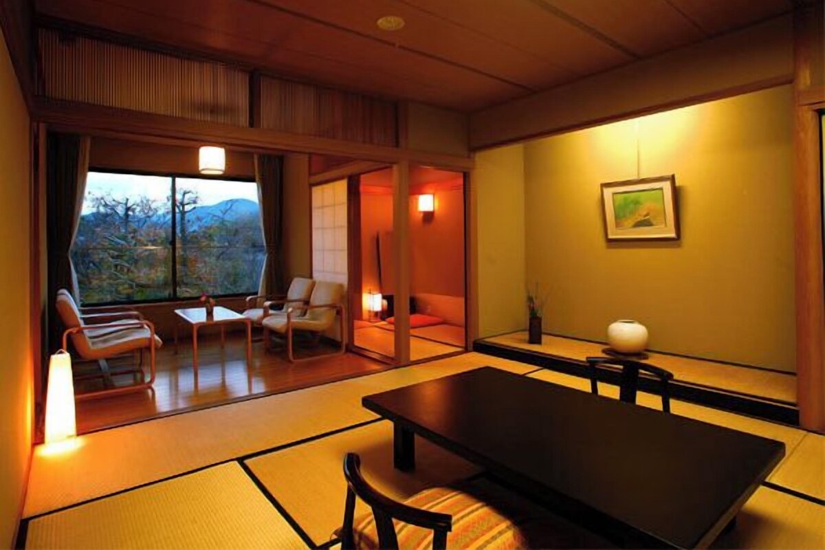 Une pièce de style japonais traditionnel, avec un sol recouvert de tatamis, une table basse et une vue sur l’extérieur.