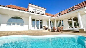 A swimming pool with a tiled deck, a covered patio area with outdoor furniture, and a building with a tiled roof and large windows. - Beach Resort Chikura (Minamiboso)
