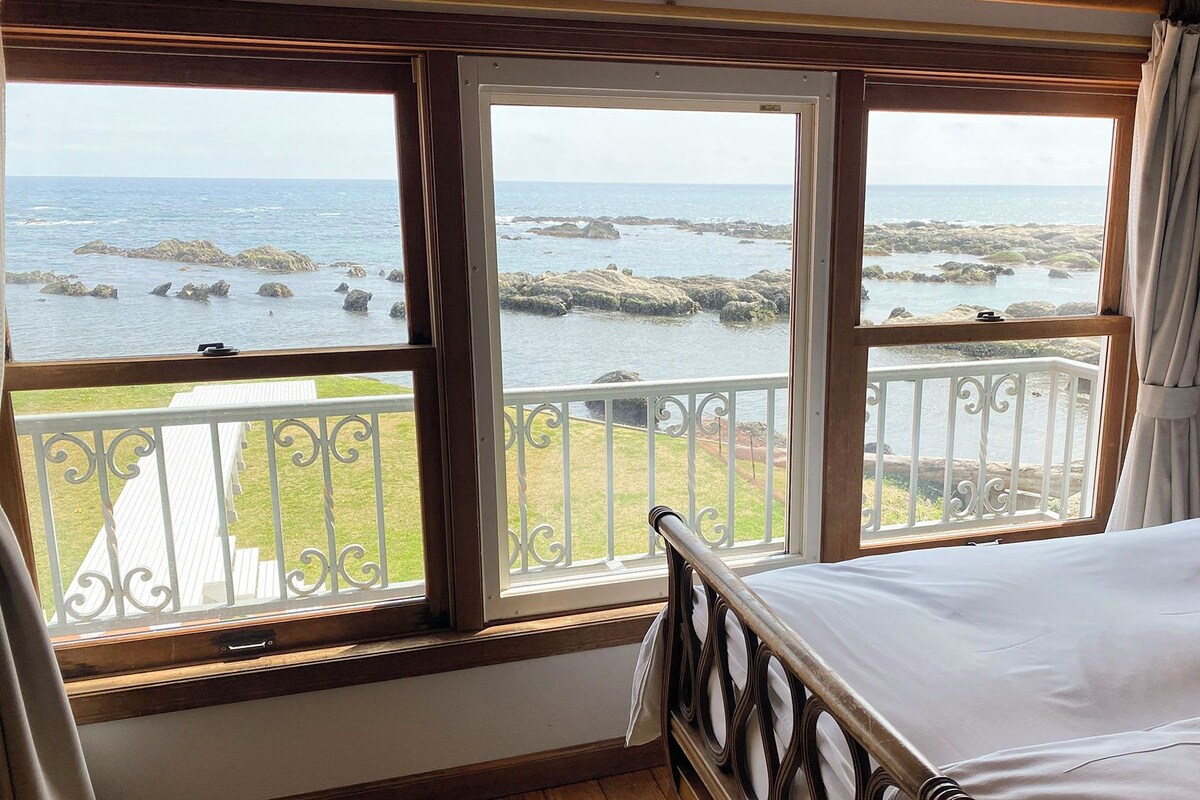 Une chambre à coucher avec un lit, une fenêtre donnant sur la mer et un balcon avec une balustrade.