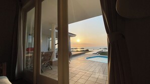 A view from a room with a sliding glass door leading to a patio with a swimming pool and a sunset over the ocean. - Beach Resort Chikura (Minamiboso)