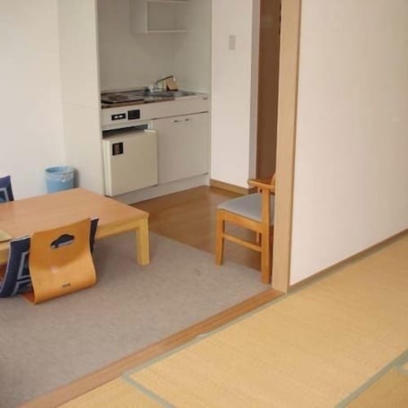 A room with a wooden dining table and chairs, a kitchen area with a stove and cabinets, and a wooden floor.