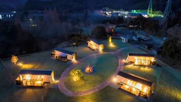 A well-lit outdoor area with multiple buildings, a central fire pit, and a parking lot.