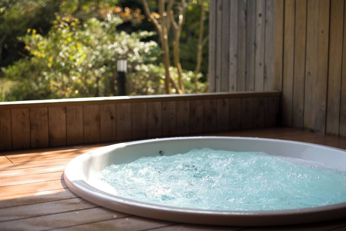 Un jacuzzi con muelle de madera y vista a árboles al fondo.