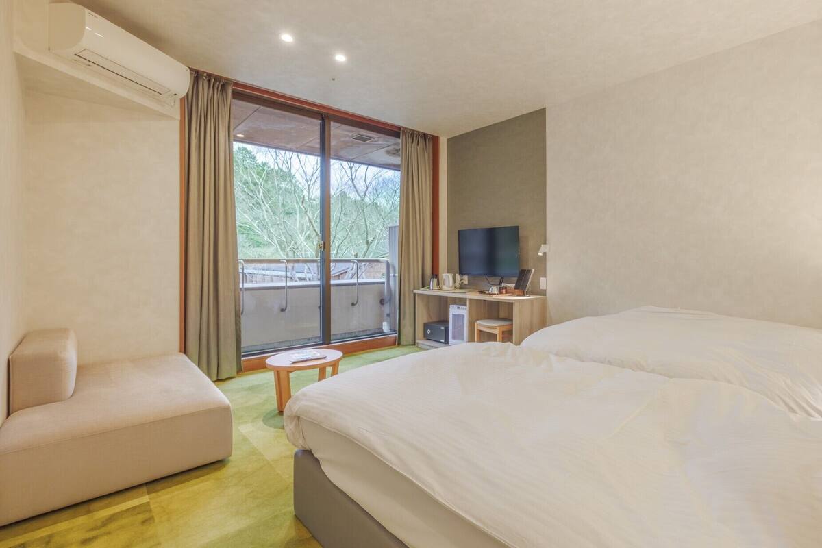 Habitación de hotel con dos camas, un escritorio con televisor, un sofá y un balcón con cortinas.
