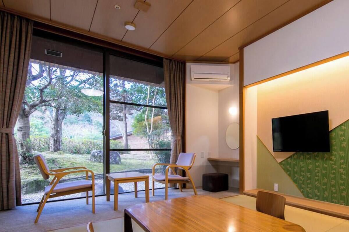 Habitación de hotel con un ventanal grande, un televisor de pantalla plana en la pared, una mesa de madera y una silla.