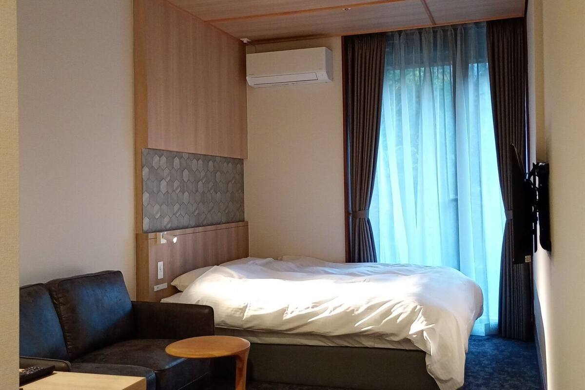Habitación de hotel con cama, sofá, una mesita, aire acondicionado y ventana con cortinas.